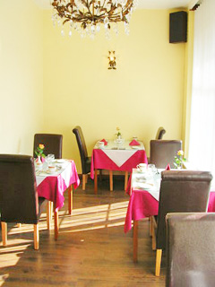 Legends Hotel dining room showing tables on the left and right with pink cloths and glass table tops. Chandeliers hang from the ceiling.